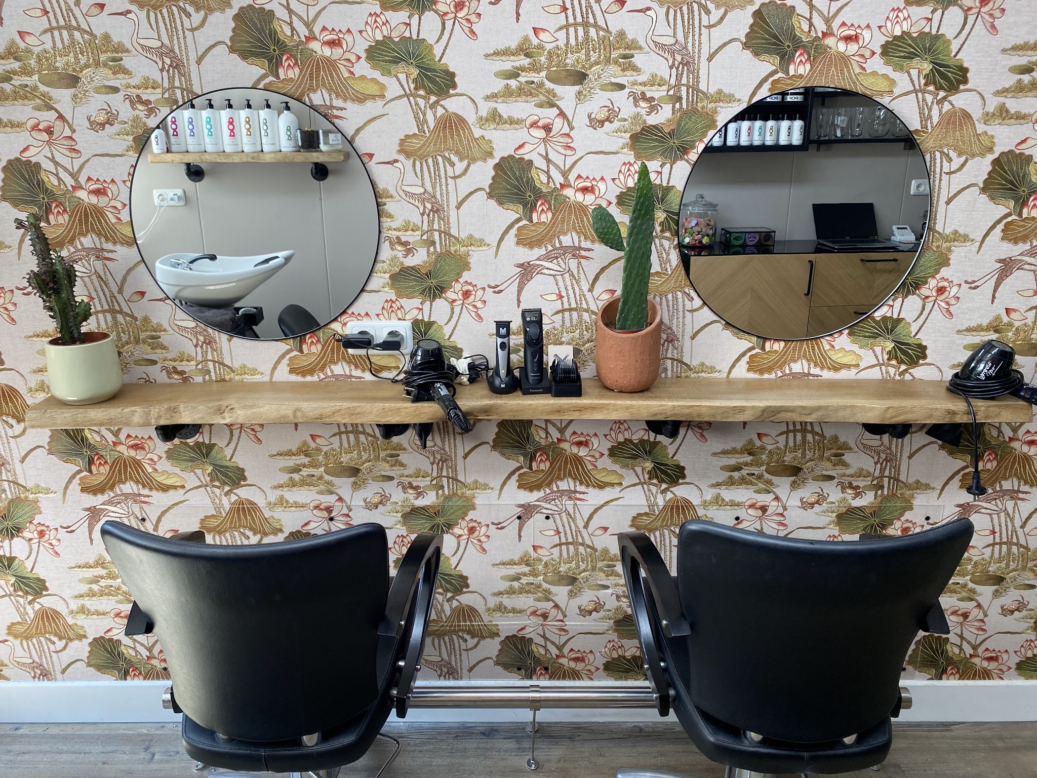 De salon van Haarstudio 16 met botanisch behang, twee ronde spiegels en twee stoelen